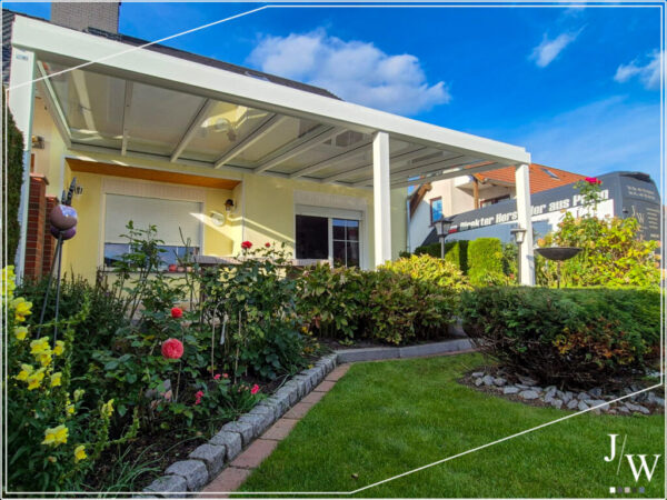 Helle Terrassenüberdachung aus Aluminium an einem gelben Einfamilienhaus, moderne Konstruktion im gepflegten Garten - hochwertige Ausführung von JW Company