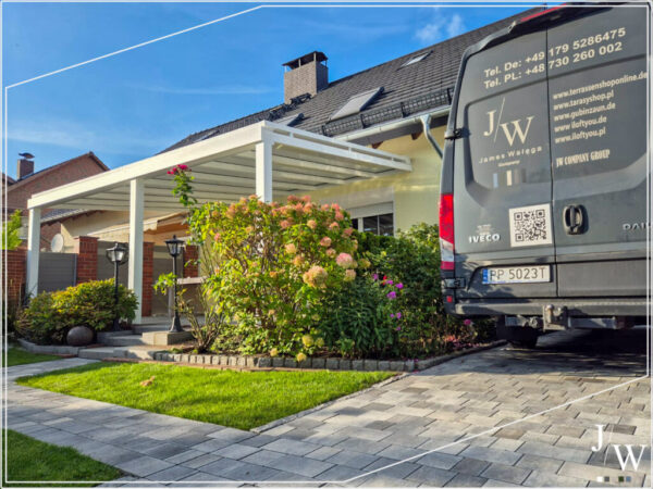 Weiße Aluminium Terrassenüberdachung an Einfamilienhaus, umgeben von gepflegtem Garten und Einfahrt, professionelle Montage durch JW Company