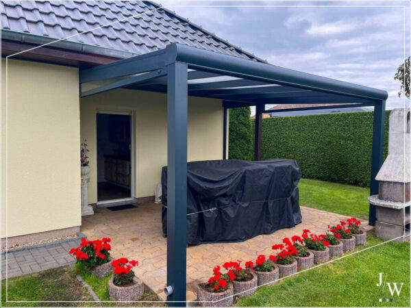 Terrassenüberdachung aus Aluminium in Anthrazit an der Hauswand montiert, mit überdachtem Sitzbereich und Blick auf den grünen Garten mit Blumenkübeln