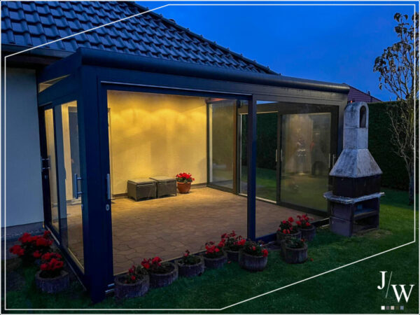 Moderner, beleuchteter Wintergarten mit Glaswänden am Einfamilienhaus – gemütlicher Außenbereich für Abende im Garten