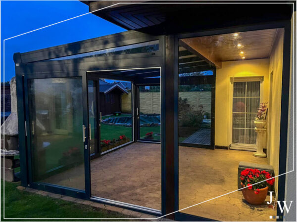 Beleuchteter Wintergarten mit modernen Glasschiebetüren und Blick auf den Garten – gemütliche Erweiterung des Wohnraums für jede Jahreszeit