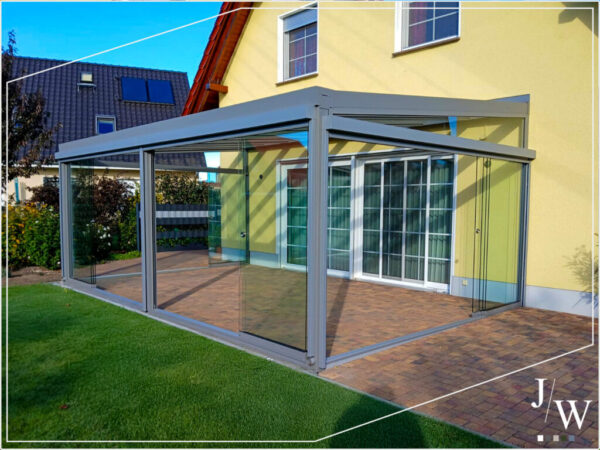 Terrassenverglasung als erweiterter Wohnraum: rahmenloses Glassystem, Pflasterbelag und Rasen am modernen gelben Haus in Eisenhüttenstadt