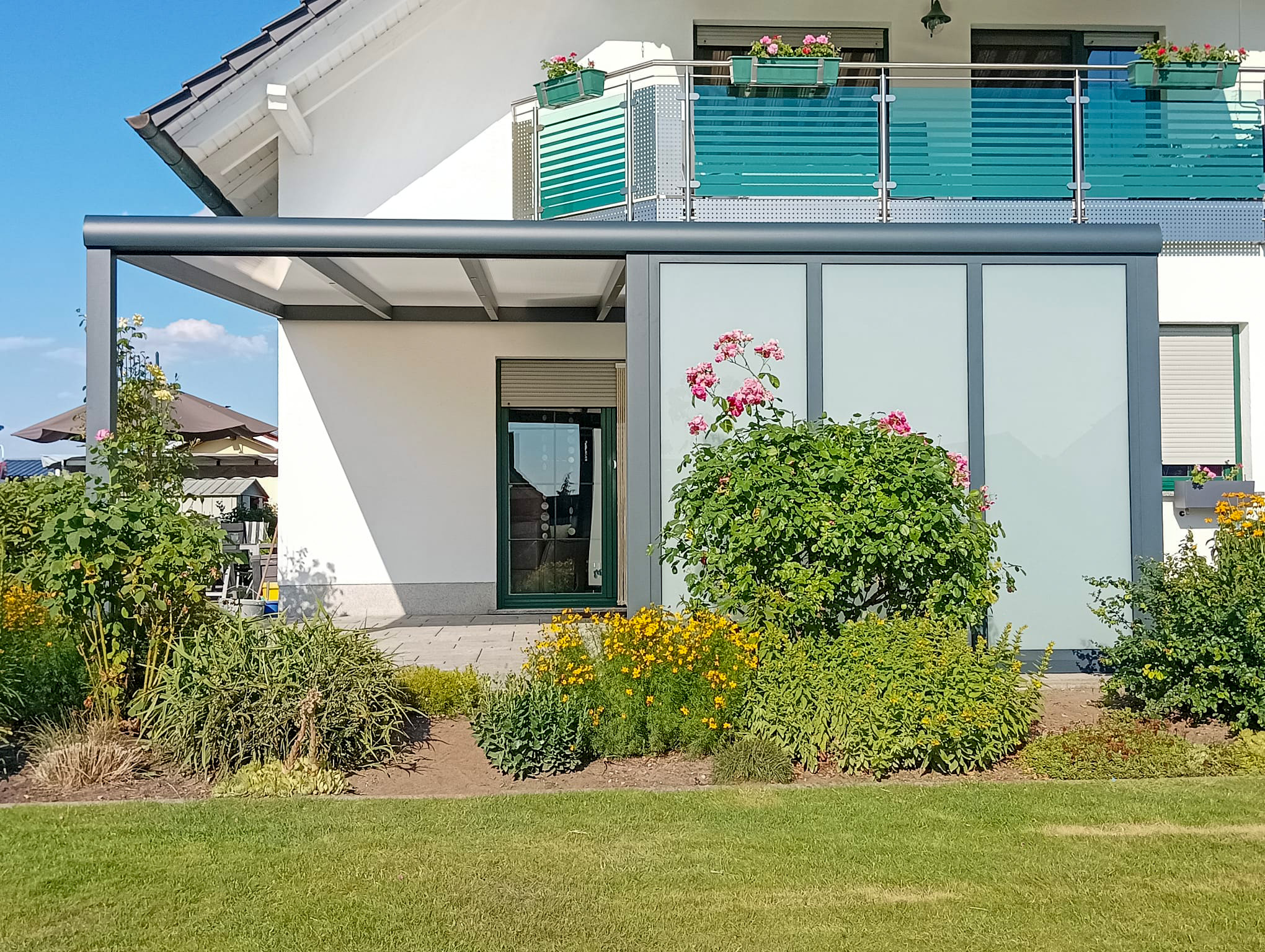 Moderne Terrassenüberdachung in Dreiheide mit milchweißer Verglasung an einem weißen Haus im Grünen